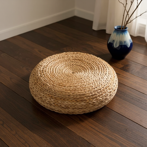 Woven floor cushion on a wooden floor with a vase in the background