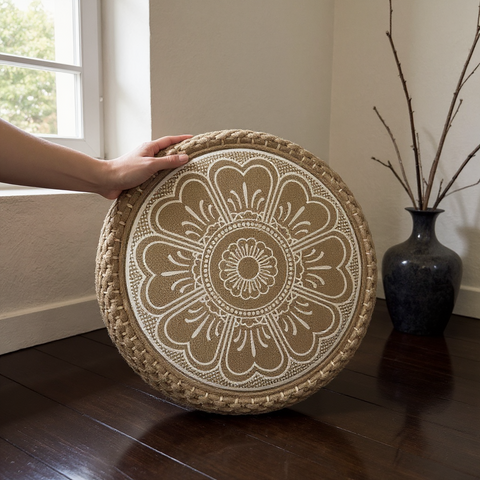 Round decorative cushion with intricate patterns held by a hand on a wooden floor.