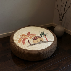 Round woven cushion with a tropical design on a wooden floor.