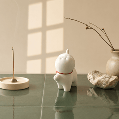 White ceramic piggy bank with a red ribbon on a green surface, surrounded by minimal decor.
