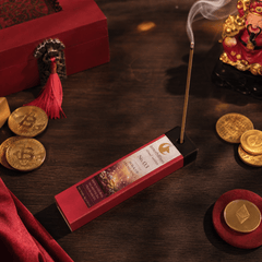 Incense stick with packaging on a wooden surface with coins and figurines.