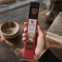 Hand holding a red incense stick box labeled 'innerbillion' on a wooden surface with an incense burner in the