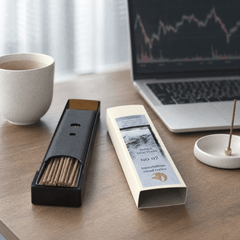 Incense stick holder with incense sticks on a desk next to a laptop and mug.