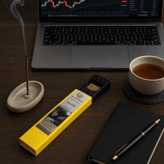 Incense stick box with incense sticks, a laptop, cup of tea, and writing utensils on a wooden surface.