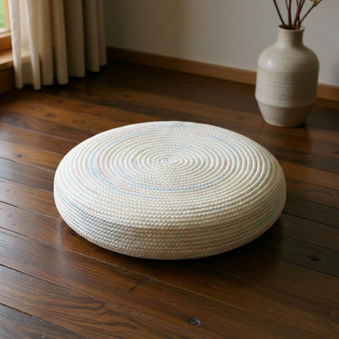 Round woven cushion on a wooden floor with a vase in the background