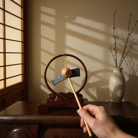 Person holding a wooden tool near a decorative chime on a wooden surface 