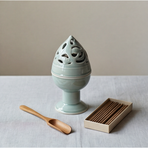 Ceramic incense burner with wooden scoop and incense box on a light surface