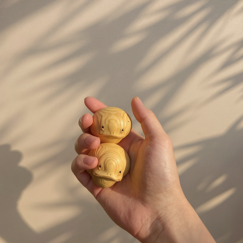 Hand holding two wooden toys against a neutral background