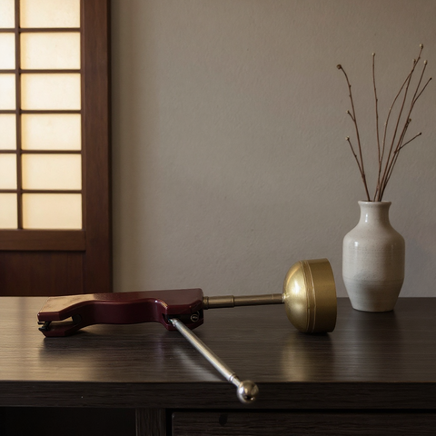 Decorative Handbell on a wooden surface with a vase and branches in the background.